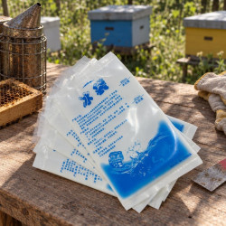Gel ice packs stacked on a wooden table near beehives and beekeeping tools