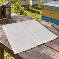 Hive cover cloth on a wooden apiary table near a smoker, brush and hives