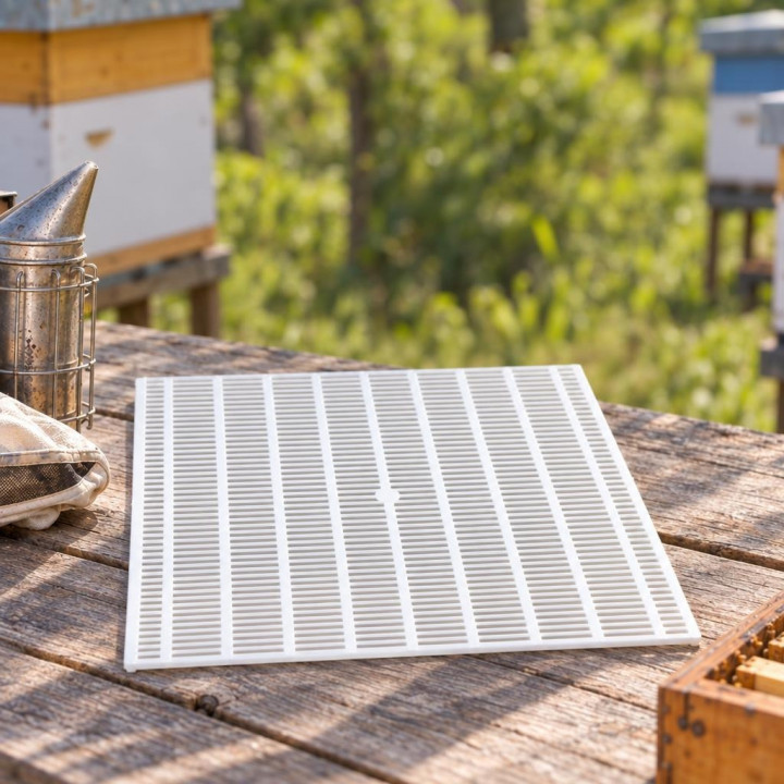 White queen excluder on a wooden table at an apiary, with smoker and hives nearby