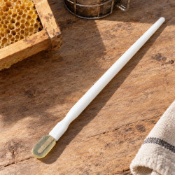 White royal jelly spatula on a wooden table beside a honeycomb frame